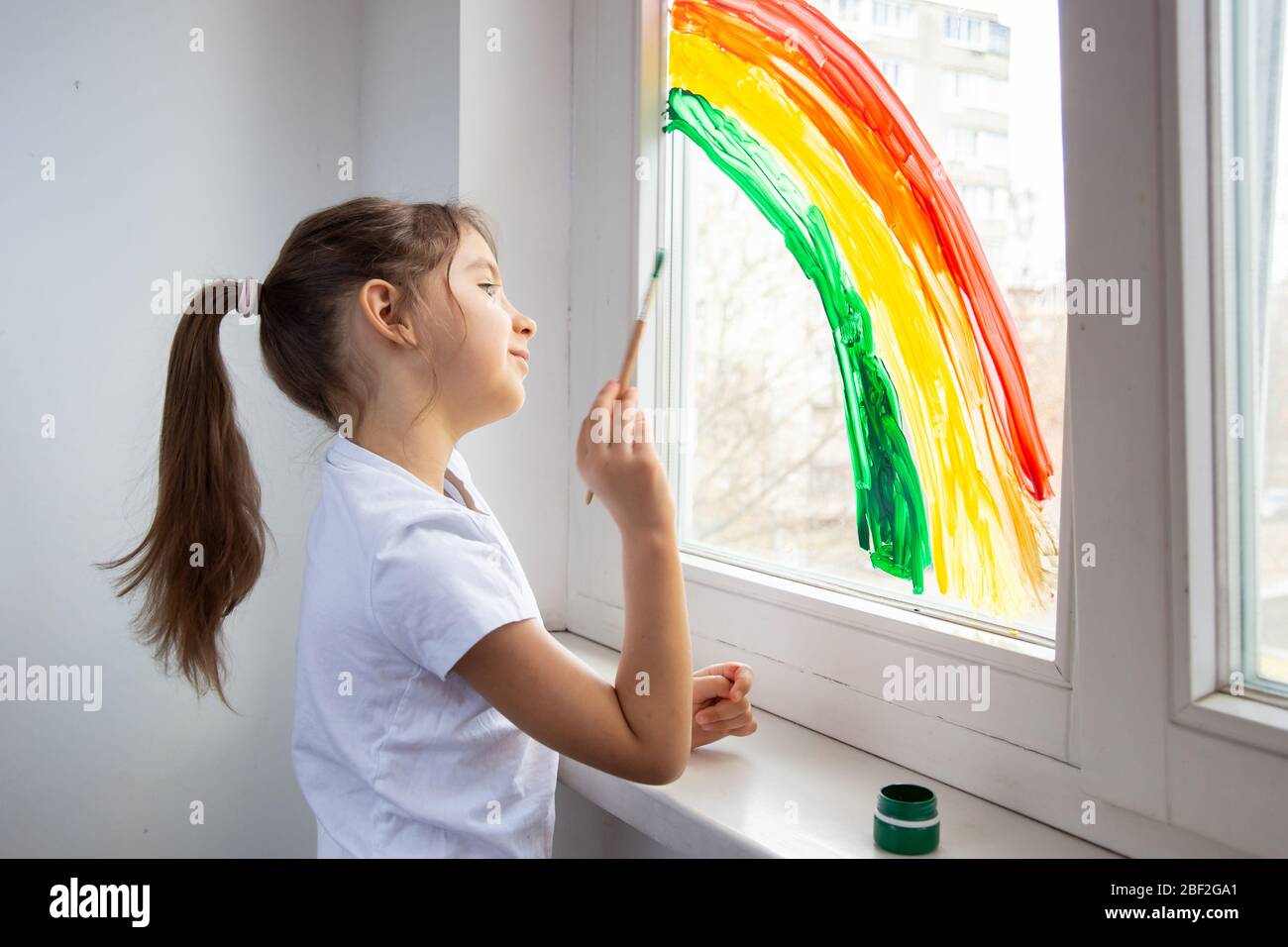 Das Kind zeichnet einen Regenbogen auf das Fenster, um zu zeigen, dass alles gut wird. Jagt den Regenbogen-Fashmob. Quarantäne während eines Pandemiekonzepts. Innen Stockfoto