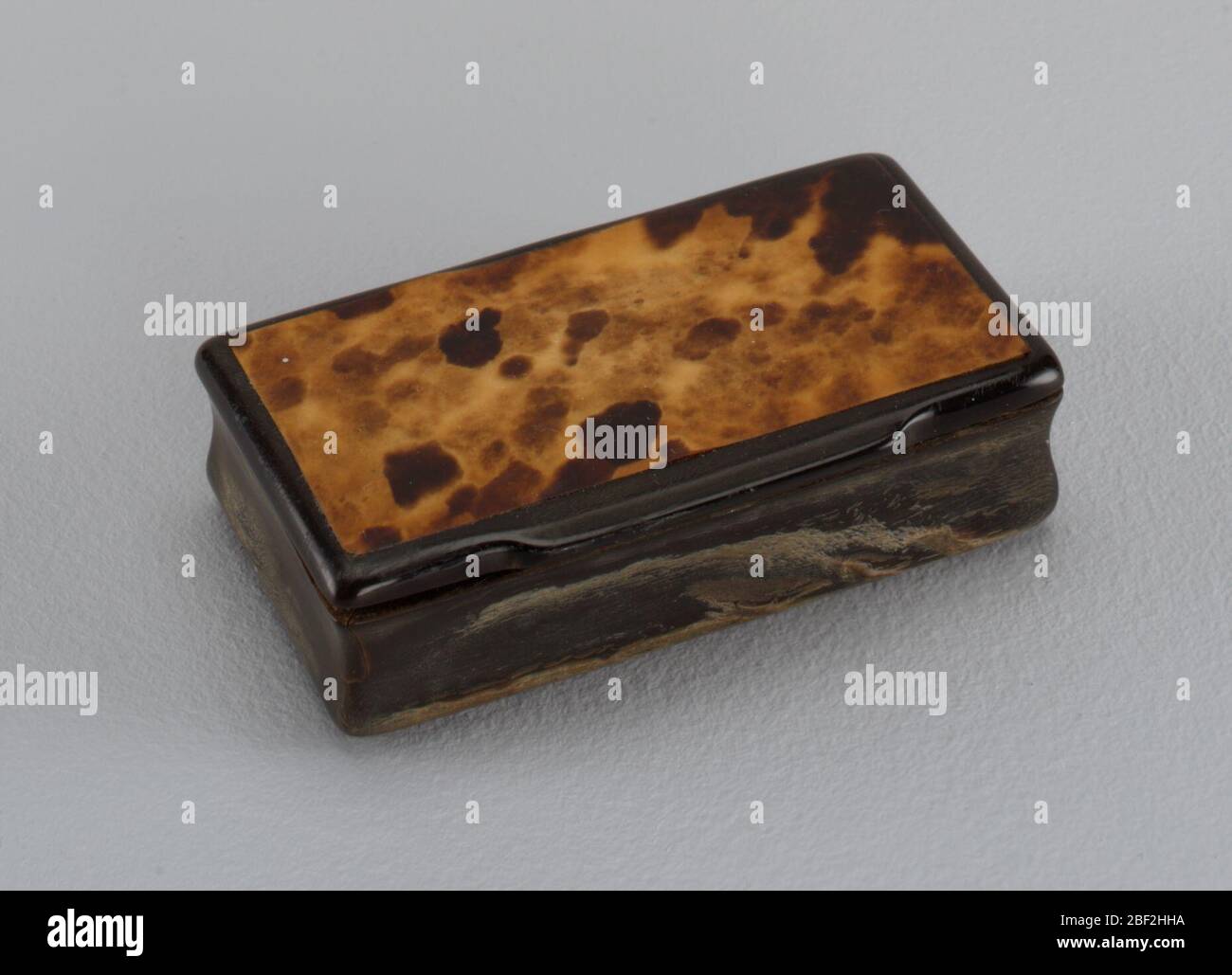 Box mit Klappdeckel. Kleine rechteckige Box aus Knochen, schwarz mit Klappdeckel und dünnen Furnier aus Schildkrötenschale auf Deckel. Die Seiten des Kastens sind von oben nach unten gebogen (konvex, konkav, konvex) Stockfoto