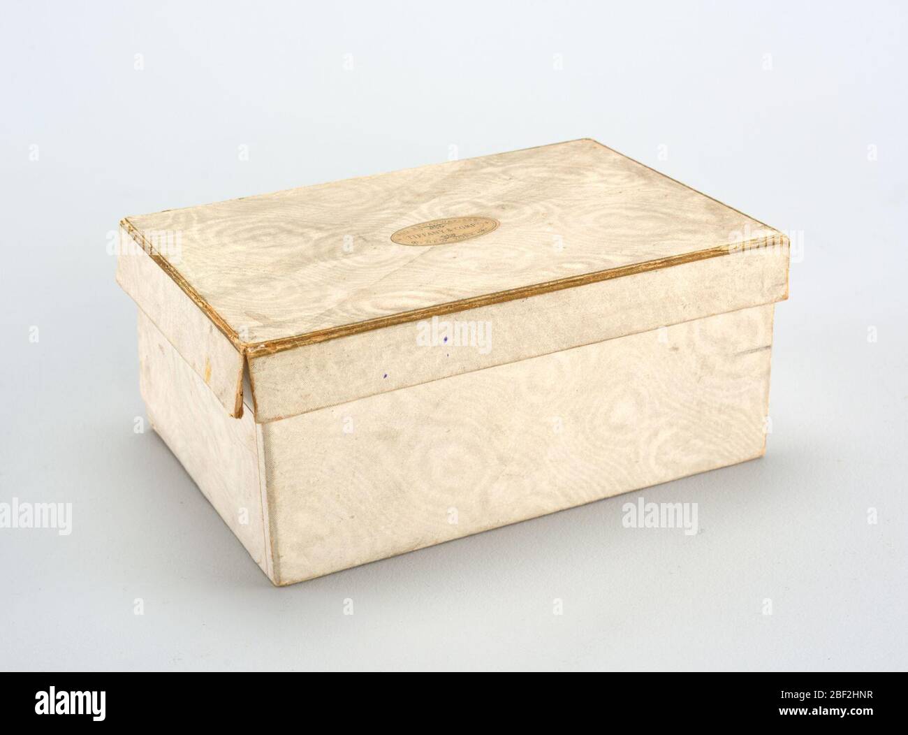 Karton und Deckel. Rechteckige Box mit wässriger weißem Papier bedeckt. (B) Einband, außen mit bewässertem Papier, Kanten mit Goldpapier umrandet. Ovales Etikett auf der Oberseite '550 Broadway 552 + Tiffany Compy + New York.' Innen großes Etikett in Lavendel gedruckt. Stockfoto