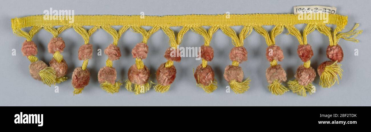 Fransen. Gelbe und rosa Fransen mit einer Überschrift und gelben Rockfäden hängen in Clustern; alle zwei Cluster zusammen gefangen und mit Ornamenten aus rosa Zahnseide verziert. Stockfoto