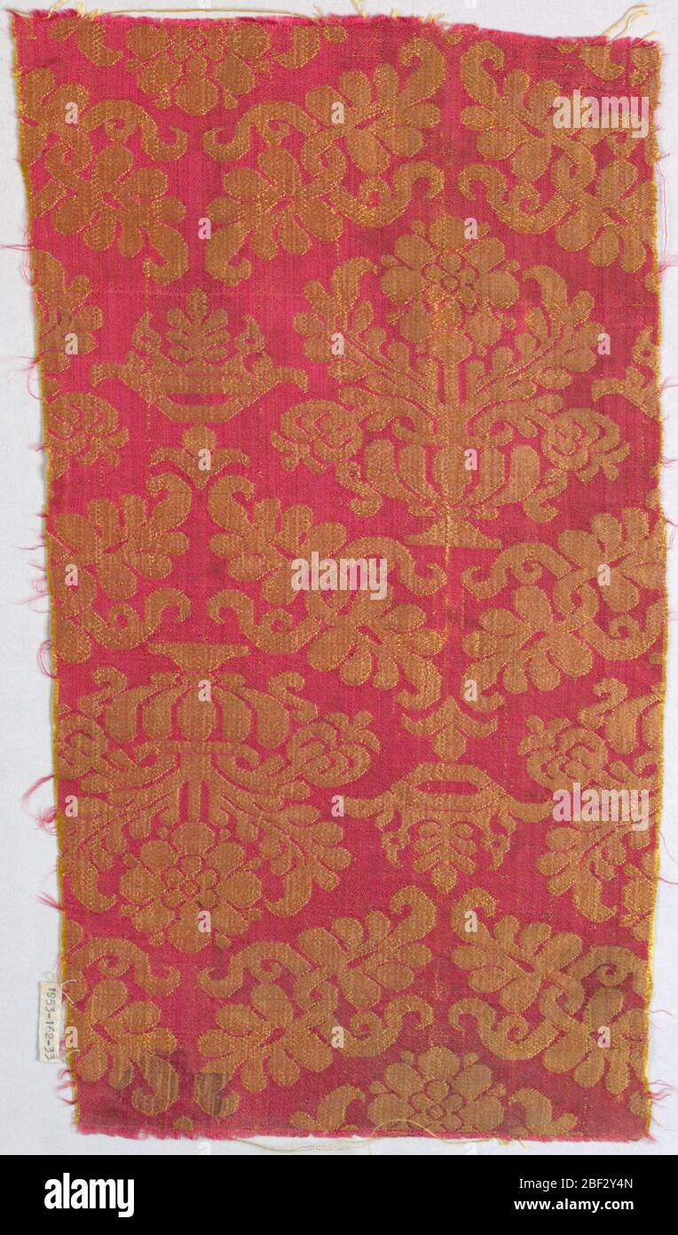 Fragment. Rötlich-brauner Damast mit einer symmetrischen, mittelmaßstäbigen Wiederholung einer Blumenvase in einem Rahmen aus kieselndem Laub. Tangenten von Ogiven, die von Kronen umspannt sind. Stockfoto