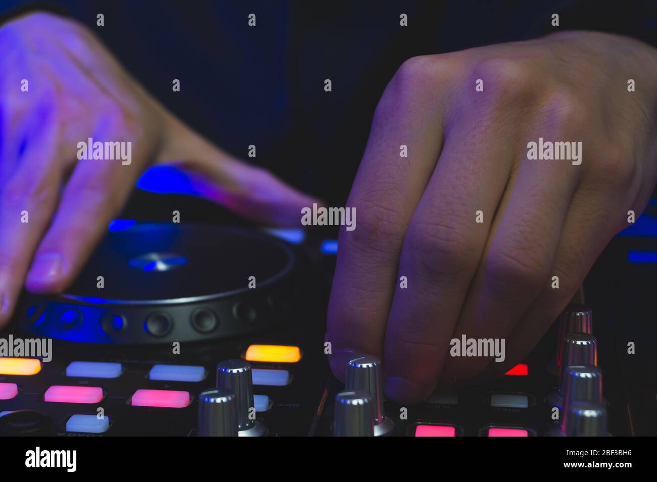 DJ spielt Musik ab. Sound Mixer Controller mit Knöpfen und Schiebereglern nah oben. Hände auf dem Mischdeck mit Drehtischen bei Dunkelheit mit beleuchteten Bedienelementen Stockfoto
