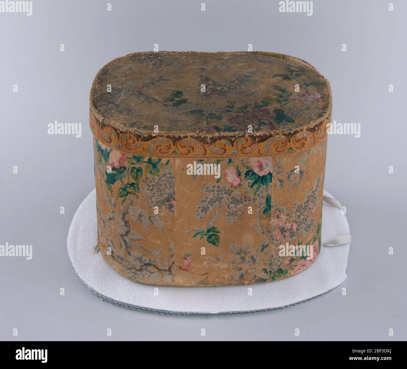 Bandbox. Inspiriert von bedruckten Chintz, ist das Design aus Flieder und Rosen in Lavendel und Rosa mit grünen Blättern auf braunem Hintergrund. Flieder in Ölfarben, Rosen und Blätter im Staupe. Auf dem Etikett auf der Innenseite des Covers steht: 'From Jesse Baker, Paper Box Manfr. Nr. 21 Bank St. Wette. Stockfoto