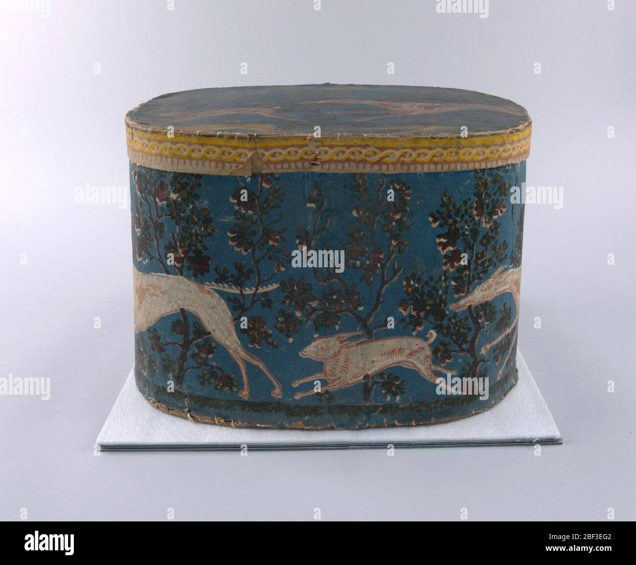 Bandbox. Blaues Feld. Greyhound jagt Kaninchen, in rosa und weiß, gegen Baumreihe, in braun, grün und weiß. Stockfoto