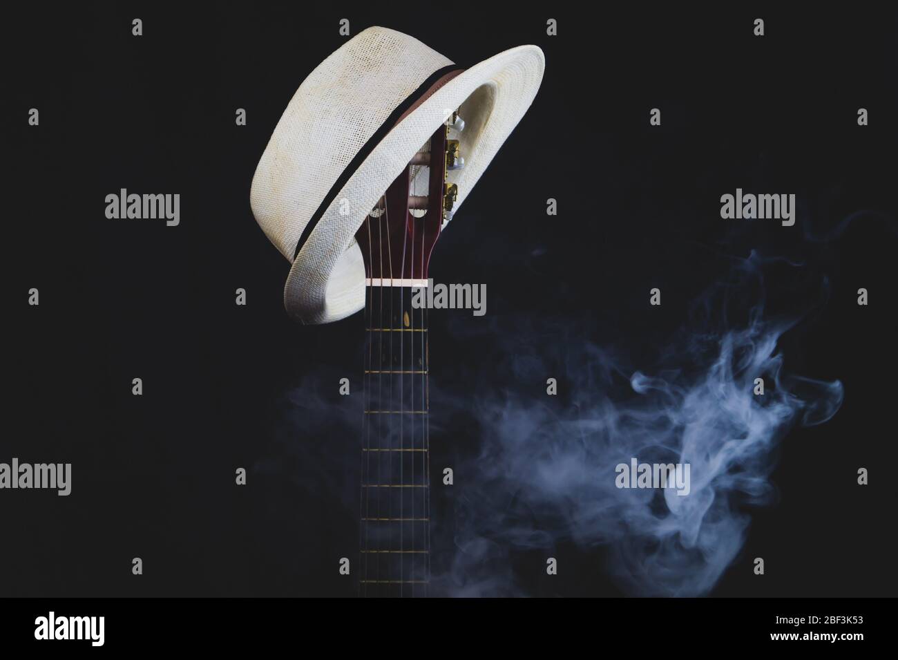 Weißer Hut hängt auf dem rauchenden Gitarrenbrett. Akustisches Musikinstrument. Saiten auf dem Gitarrenhals aus nächster Nähe Stockfoto