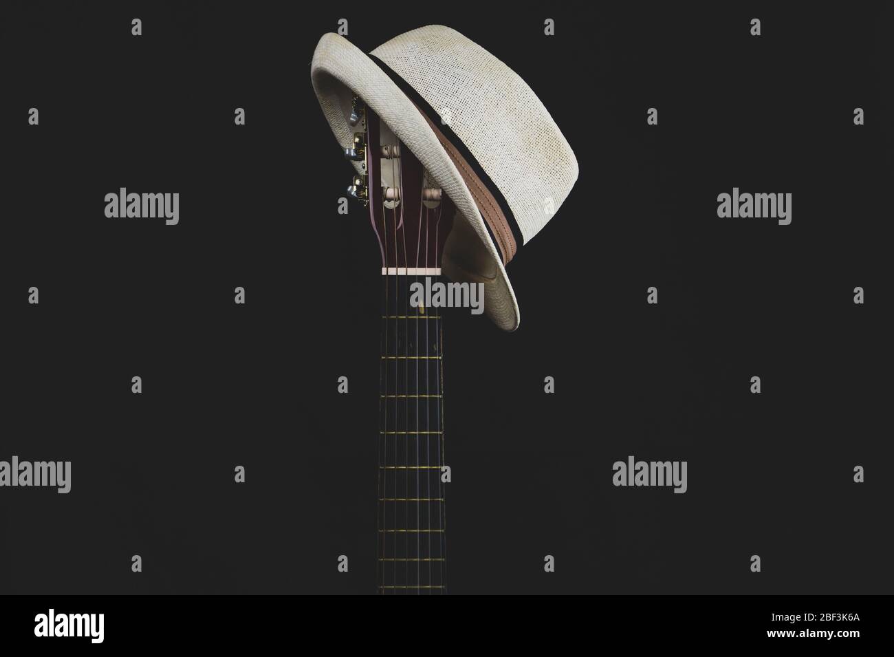 Weißer Hut hängt auf der Gitarre Griffbrett. Akustisches Musikinstrument. Saiten auf der Gitarre Hals Nahaufnahme Stockfoto