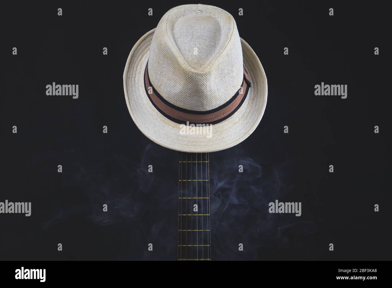Weißer Hut in Rauch hängt auf der Gitarre Griffbrett. Akustisches Musikinstrument. Saiten auf der Gitarre Hals Nahaufnahme Stockfoto