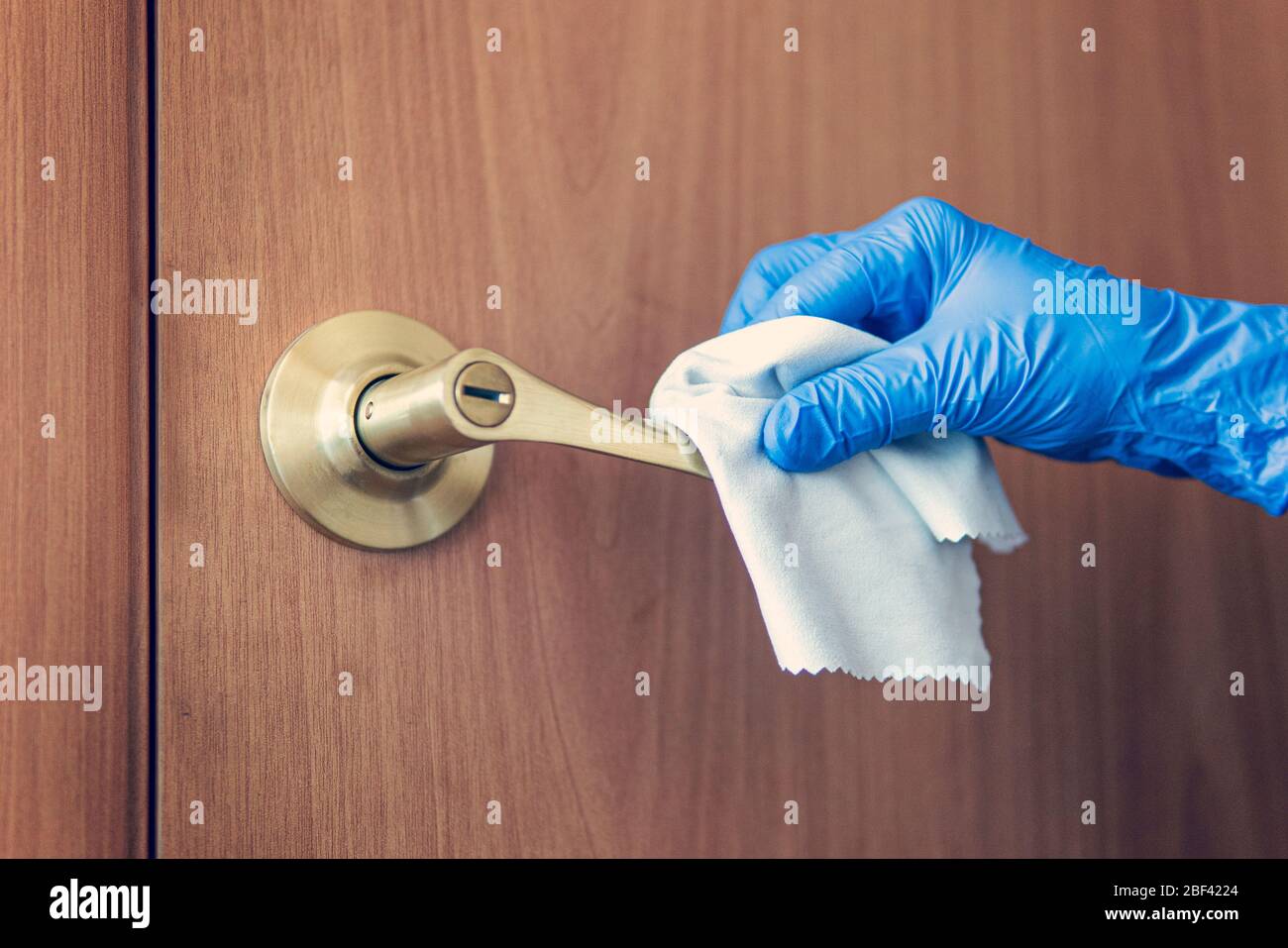 Eine Frauenhand wischt den Türgriff mit einem feuchten Lappen ab. Das Zimmermädchen wascht den Türknopf. Prävention von Coronavirus und bakteriellen Infektionen Stockfoto