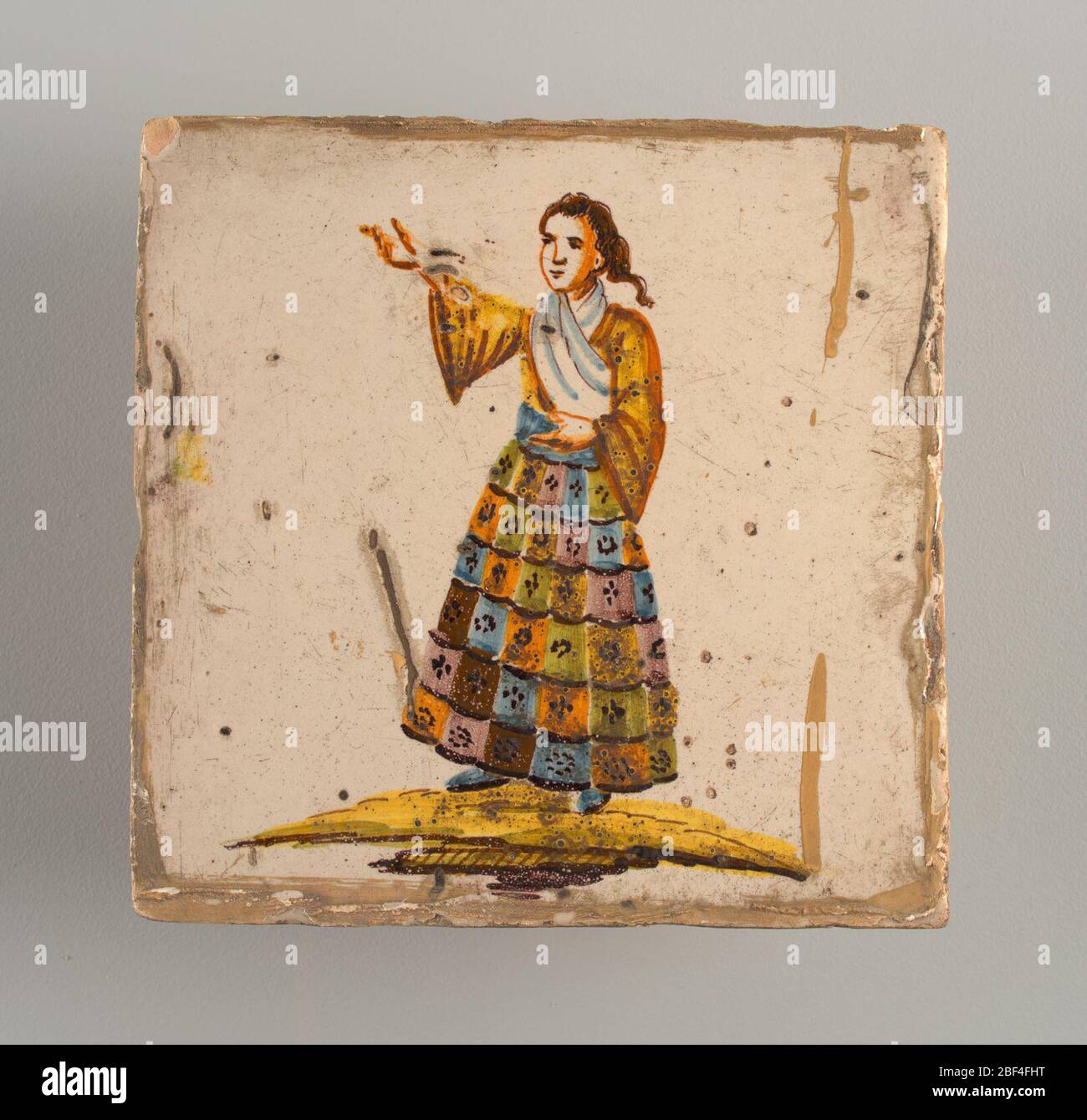Kachel. Stehende Frau, rechter Arm angehoben und zeigt auf die obere Ecke; gekleidet in mehrfarbigen karierten Rock, gelbes Hemd und weißem Schal. Dekoration im Chinoiserie-Stil. Stockfoto