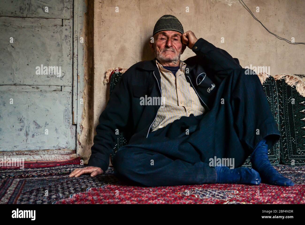 Palangan, iranisches Kurdistan - 15. November 2013: Der alte muslimische iranische Kudische, der auf dem Bodenteppich seines Hauses sitzt, schaut auf die Kamera Stockfoto