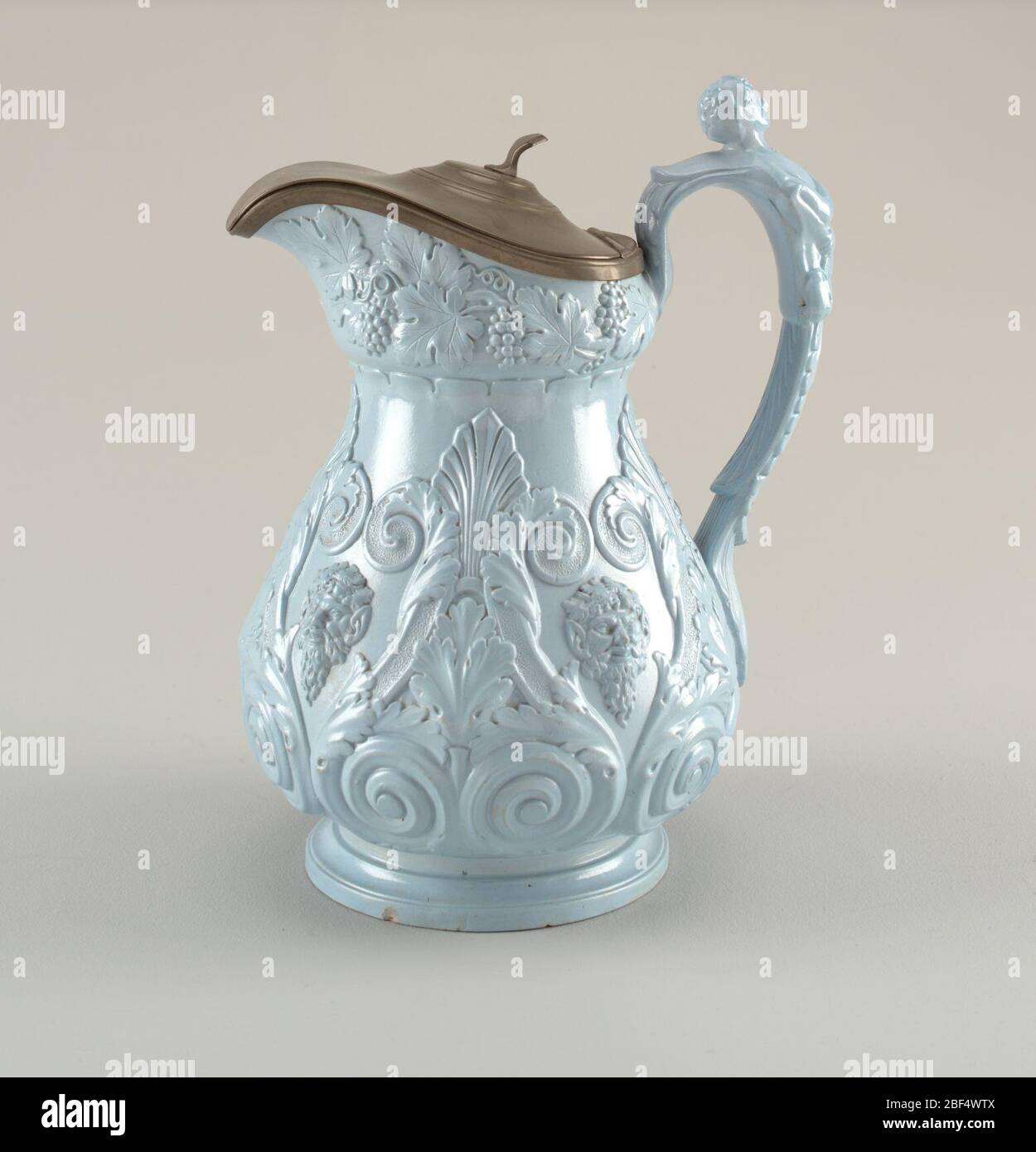 Krug. Bulbous kreisförmigen Körper mit schmalem Hals und runden Fuß. Vernickelt Deckel und Rand. Reliefverzierung aus Trauben, Volute-Rollen und Satyr-Masken. Halbe Figur am Griff. Hellblaue Glasur. Stockfoto