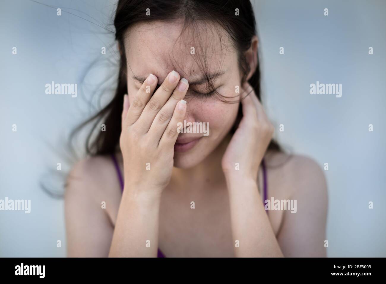 Eine Frau, die ihr Gesicht frustriert und emotional Blautöne hält. Stockfoto