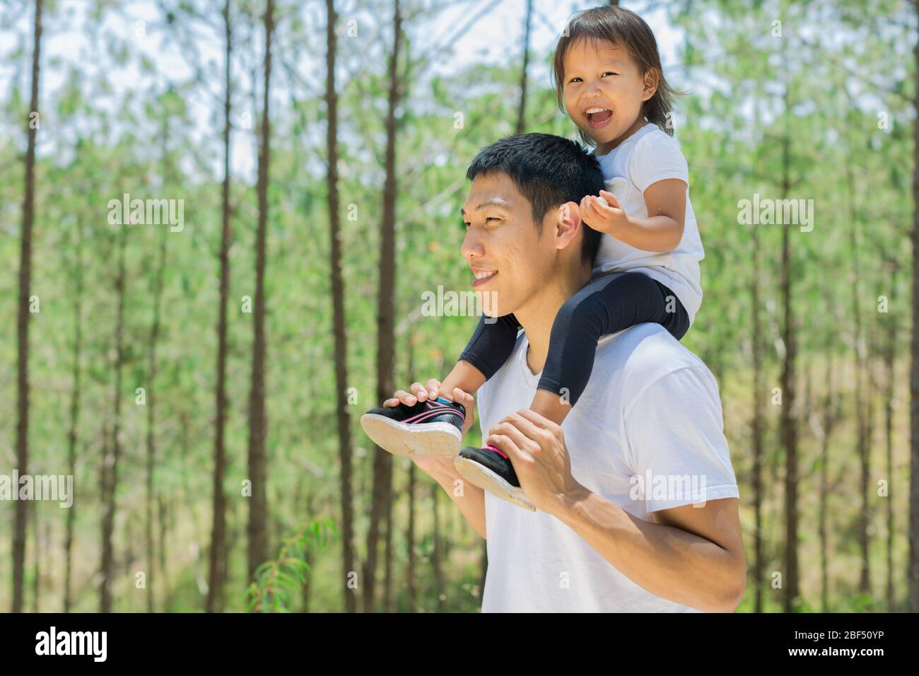 Eltern und Kinder wandern im grünen Wald. Papa fürsorgliches Kind auf seinen Schultern, Spaß haben. Lächeln und Lachen zusammen. Liebe zur Familie. Stockfoto