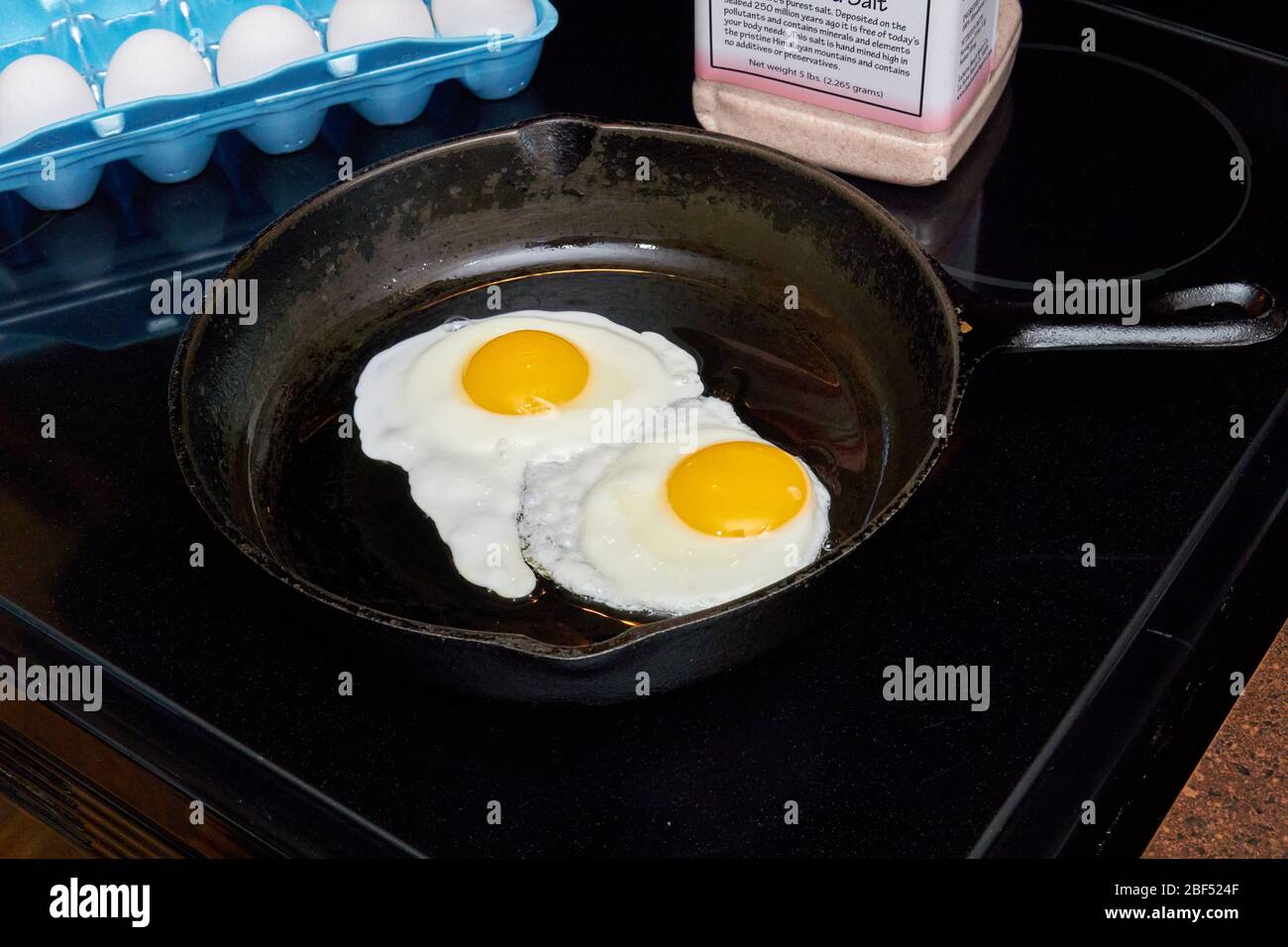 Zum Frühstück zwei sonnige Eier mit der Seite nach oben, die aus einer Gusseisenpfanne auf einem weißen Teller herausrutschen Stockfoto