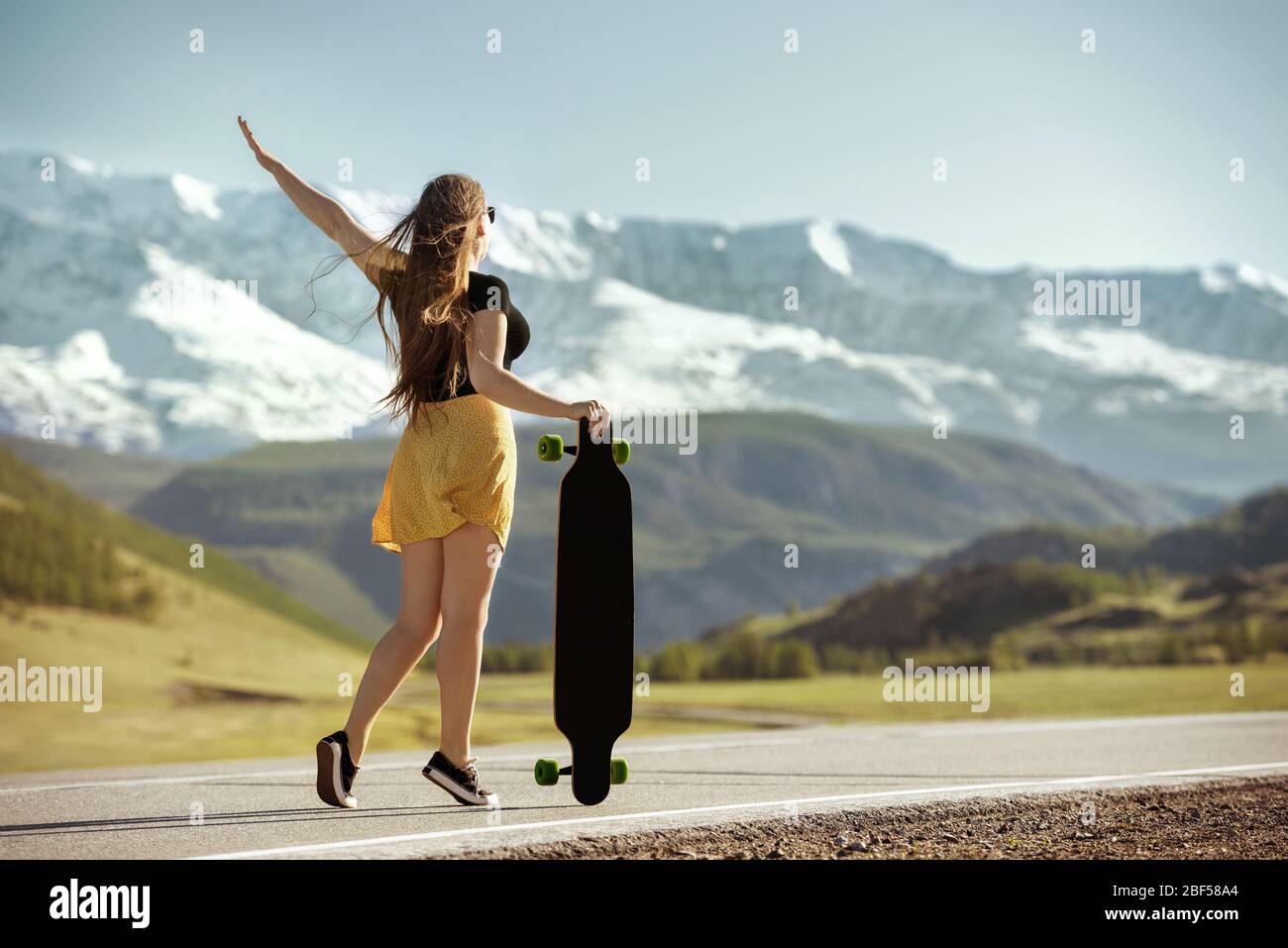 Junges Mädchen steht mit Longboard an der Bergstraße Stockfoto