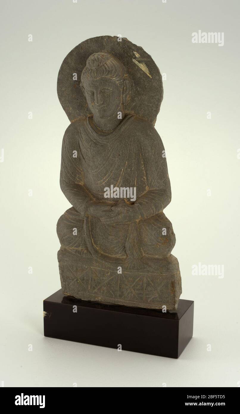 Buddha. Flache Platte aus grauem Schiefer geschnitzt, um einen gezogenen Buddha mit Halo hinter seinem Kopf zu repräsentieren, sitzend mit gekreuzten Beinen auf rechteckiger Stütze mit Händen im Schoß. Der Rückwärtsgang wird grob mit horizontalen Ausschubelinien beendet. Kleines rundes Loch in der Mitte hinten. Stockfoto