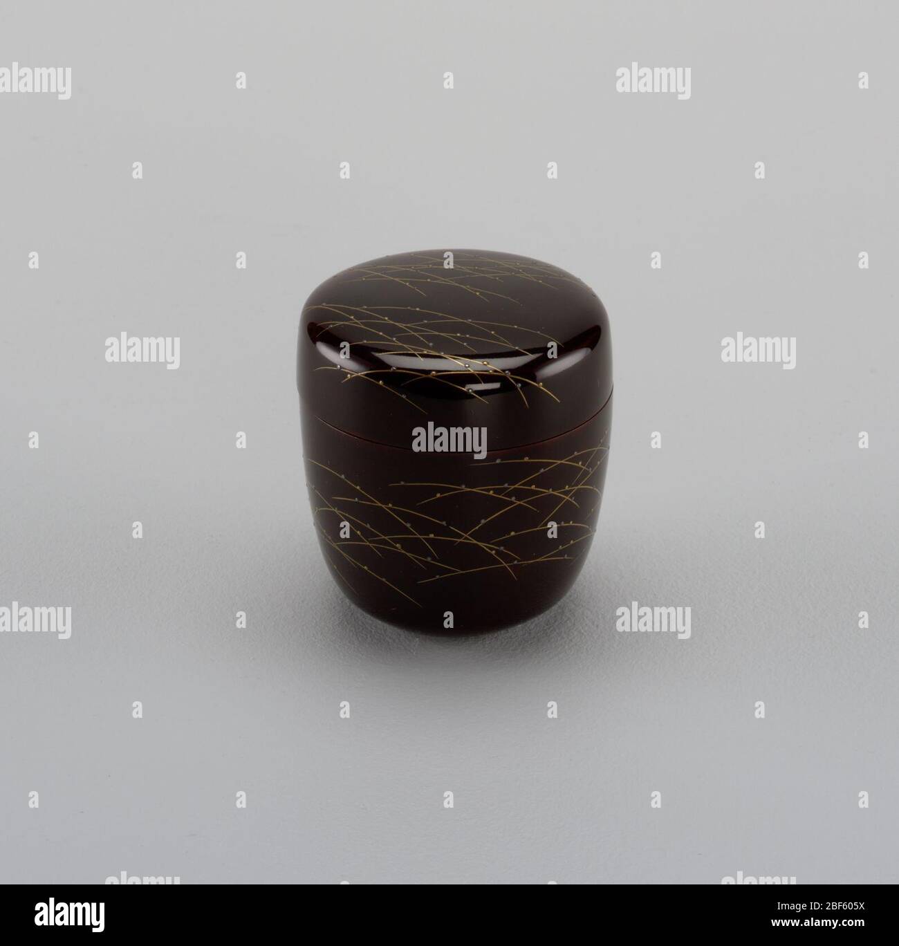 Teedose und Deckel. Zylindrische Box, unten abgerundet und leicht abfackend. Deckel flach, mit abgerundeter Kante. Brauner Lack mit Grashalmen in Gold und Reliefpunkten in Gold und Silber. Druckmarkierung unten. Stockfoto