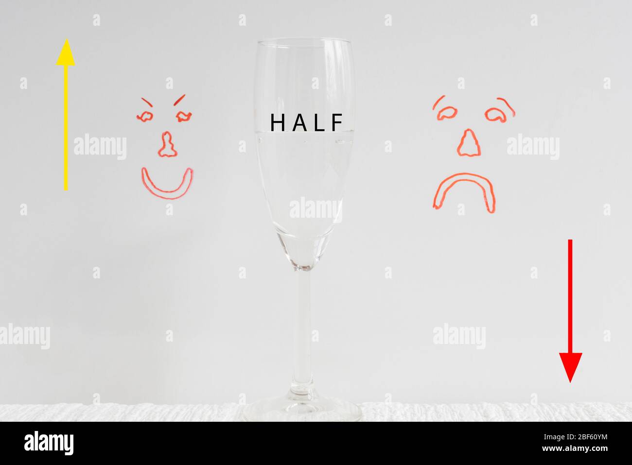 Ein Weinglas, halb voll mit aufgezogenen Pfeil nach oben/unten und traurige und glückliche Gesichter im Hintergrund, die das Konzept von Glas halb voll oder Glas halb leer darstellen. Stockfoto