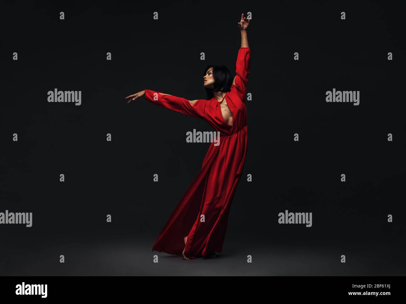 In voller Länge tanzt eine junge schöne Frau zeitgenössischen Tanz. Frau in rotem Kleid Durchführung schönen Tanz bewegt sich über schwarzen Hintergrund. Stockfoto