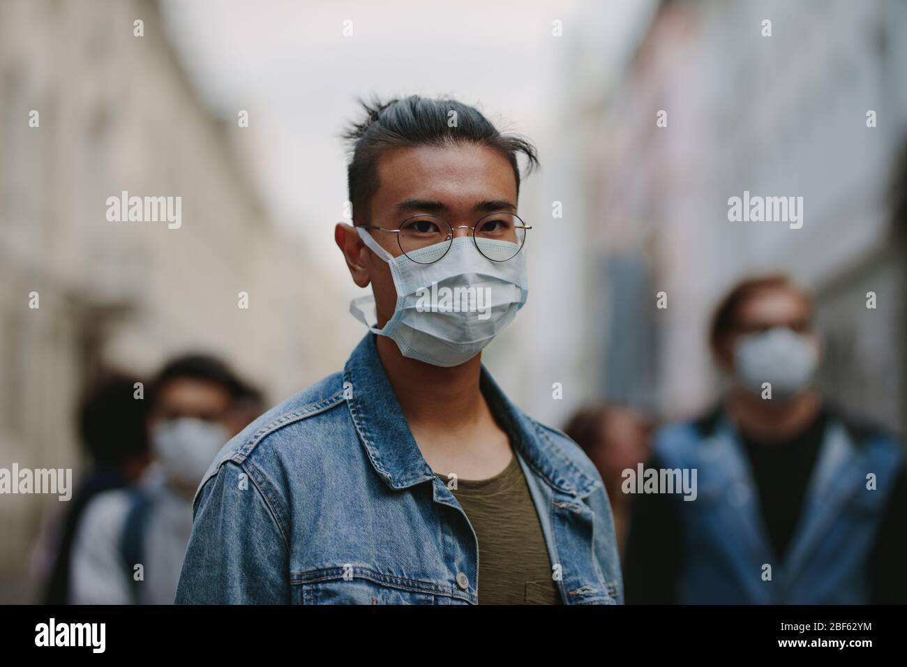 Mann, der während einer globalen Pandemie mit Coronavirus eine Gesichtsmaske trägt. Porträt eines Mannes mit einer Menschenmenge hinter ihm. Stockfoto