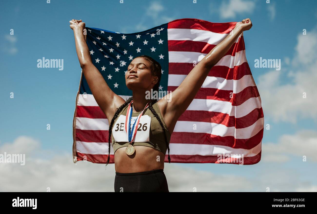 Sportlerin mit Medaille mit amerikanischer Flagge mit geschlossenen Augen. Stolze junge Frau in Sportkleidung mit US-amerikanischen Flagge. Stockfoto