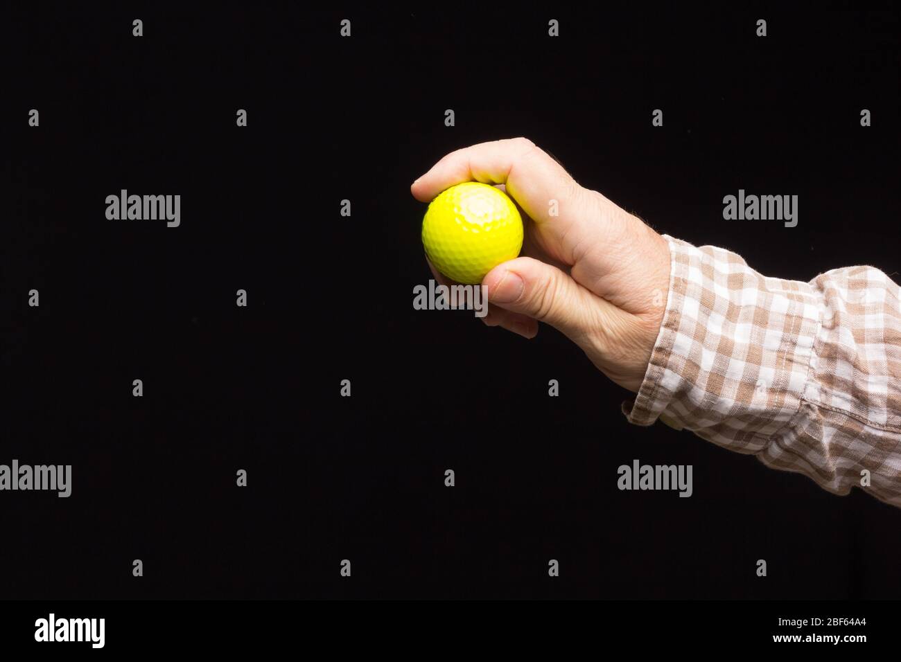 Gelber Golfball auf schwarzem Hintergrund, in der Hand eines Erwachsenen. Stockfoto