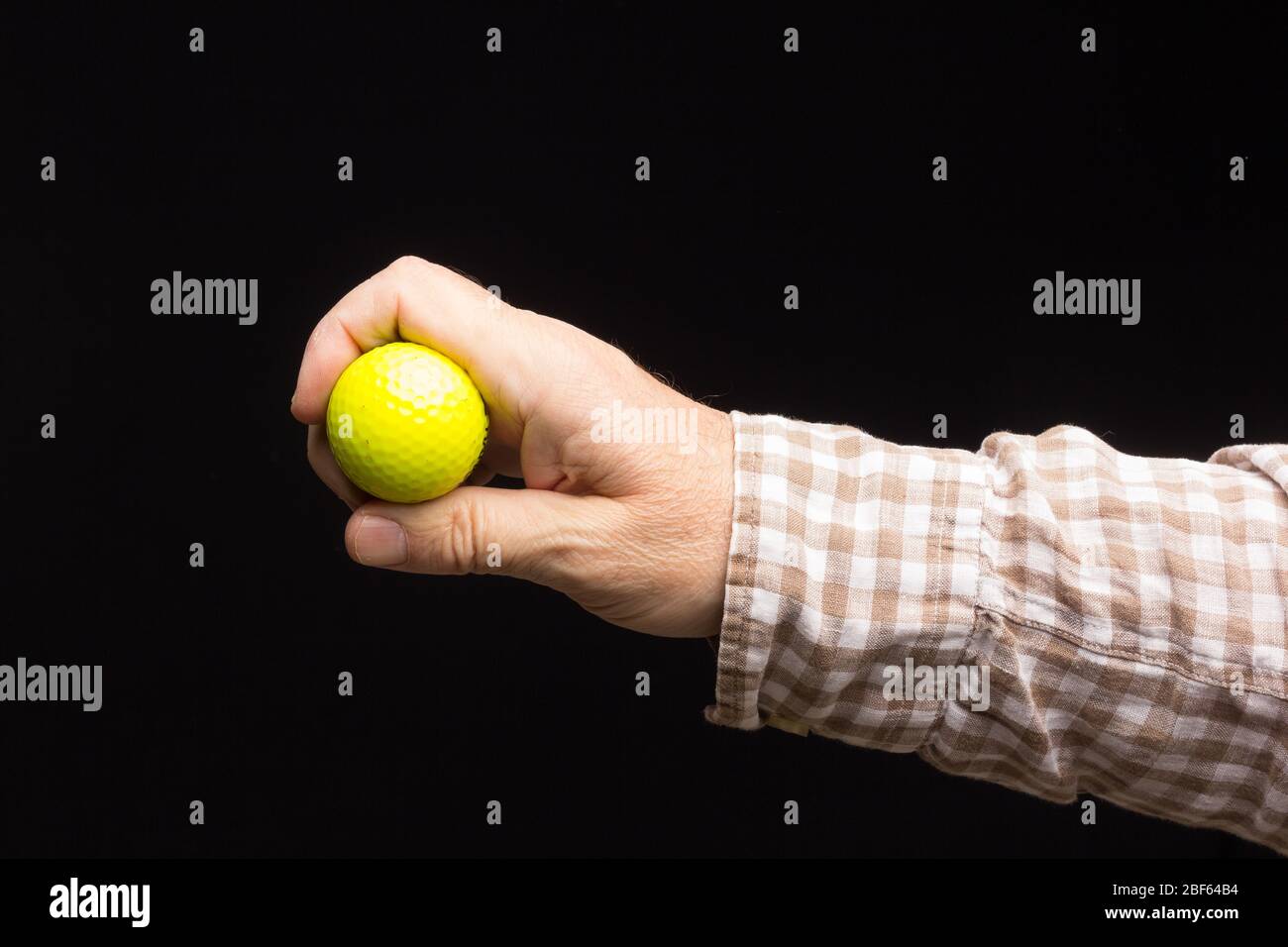 Gelber Golfball auf schwarzem Hintergrund, in der Hand eines Erwachsenen. Stockfoto