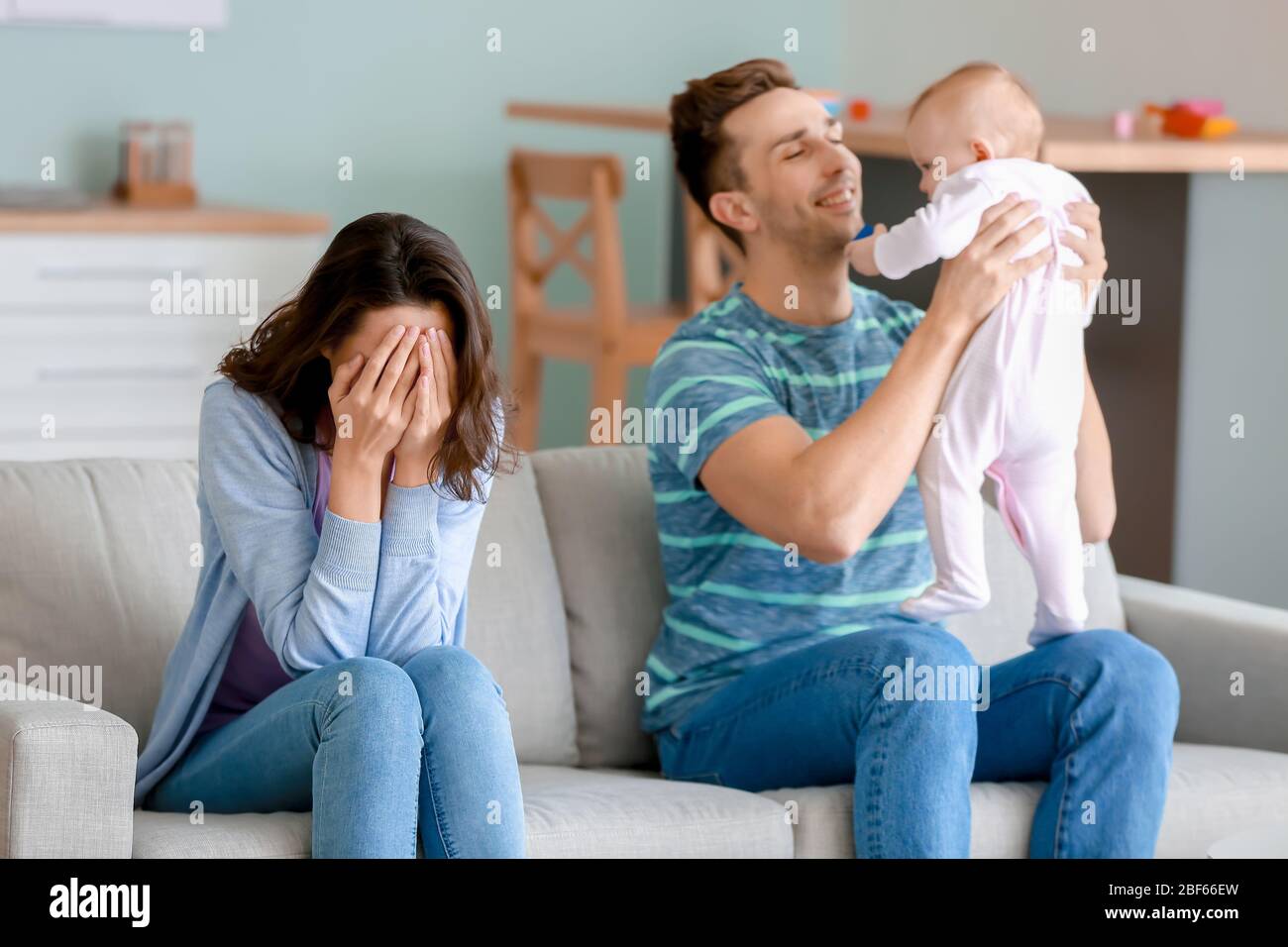 Glücklicher Vater mit seinem Baby und Frau, die zu Hause an postnataler Depression leidet Stockfoto