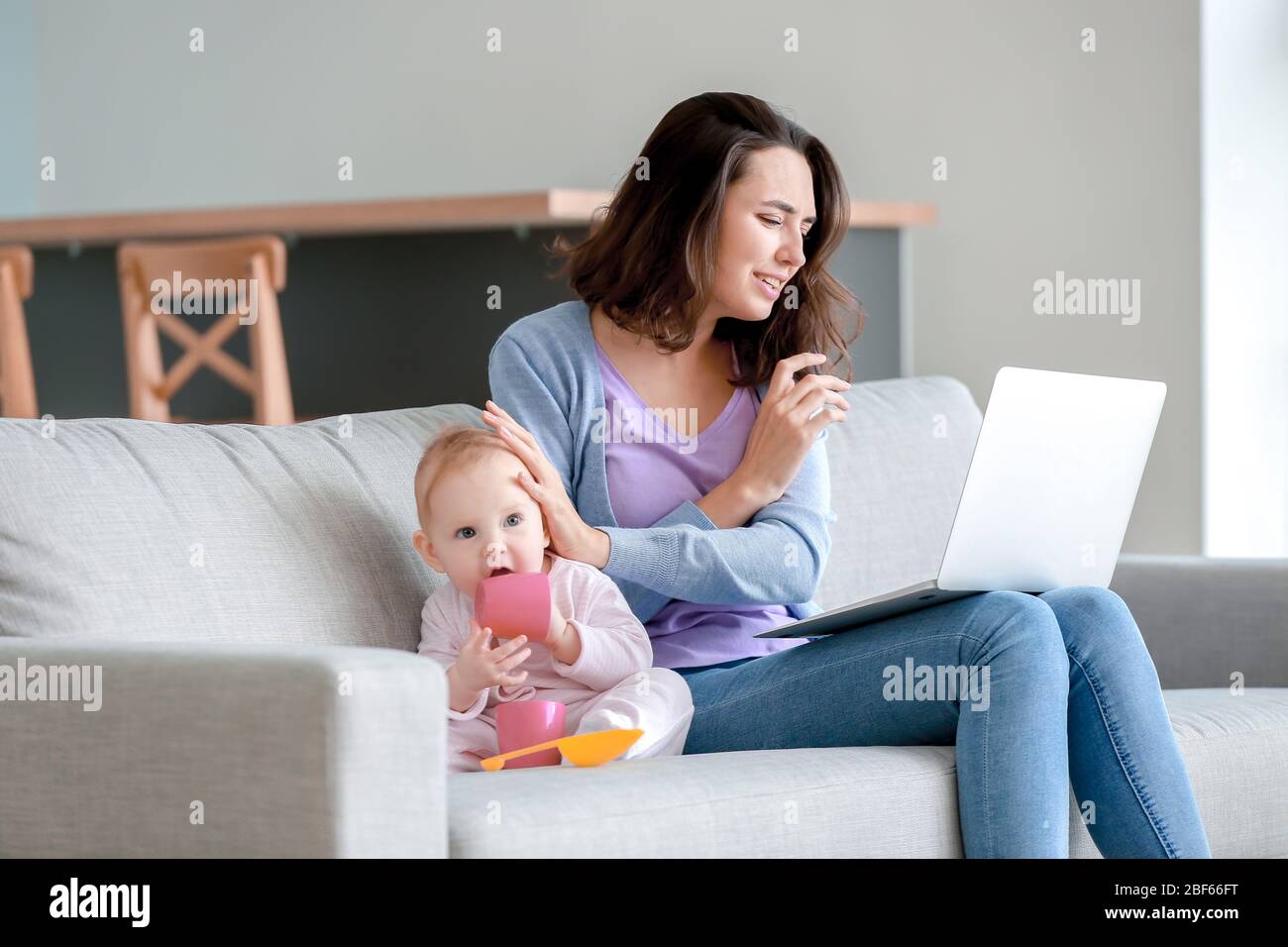 Junge Frau mit Laptop, die zu Hause an postnataler Depression leidet Stockfoto