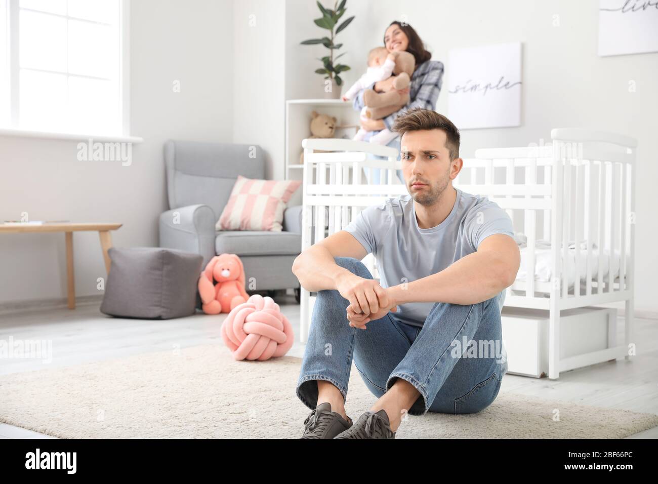 Glückliche Mutter mit ihrem Baby und jungen Vater, der zu Hause an postnataler Depression leidet Stockfoto