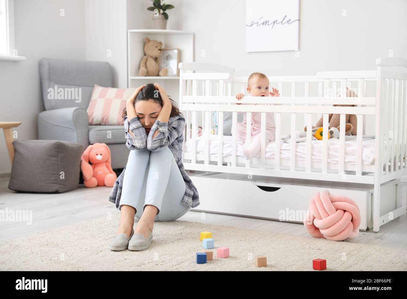 Junge Frau mit postnataler Depression in der Nähe des Bettes mit Baby zu Hause Stockfoto