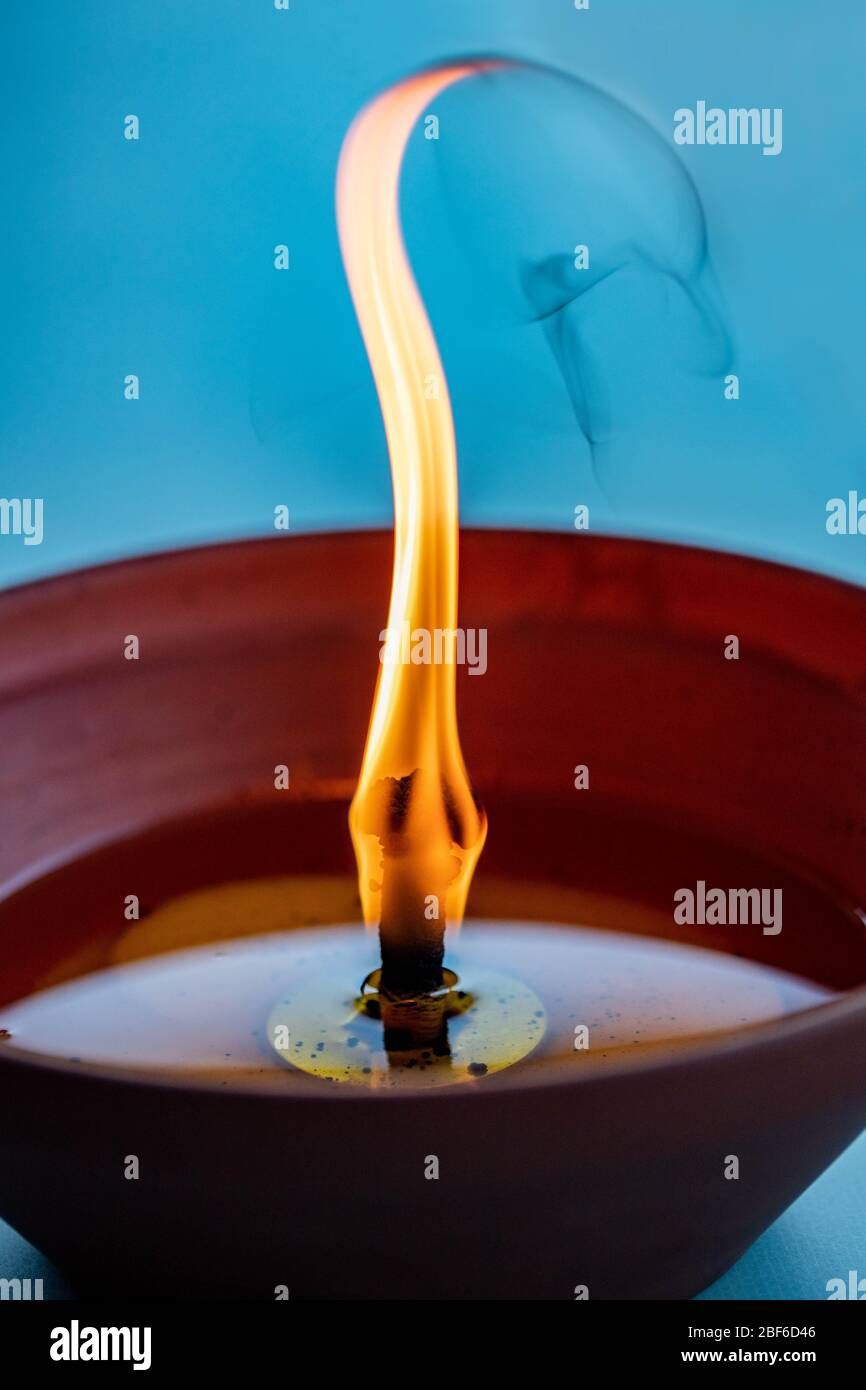 Schwankender Docht einer Anti-Mückenkerze, die in einem Tontopf aus Keramik auf türkisblauem Hintergrund brennt Stockfoto