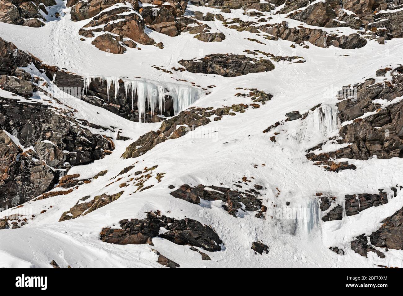Zerklüftete alpine Felslandschaft mit gefrorenem Wasserfall, der mit Schnee und Eis bedeckt ist Stockfoto