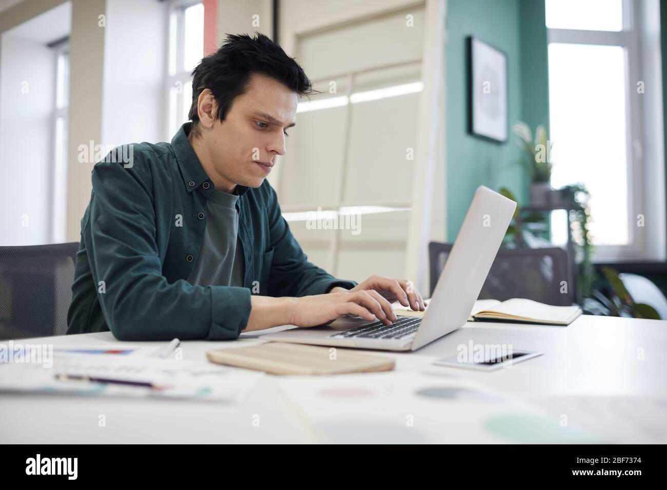 Junger Geschäftsmann in zwangloser Kleidung sitzt an seinem Arbeitsplatz und tippen auf Laptop-Computer im Büro Stockfoto
