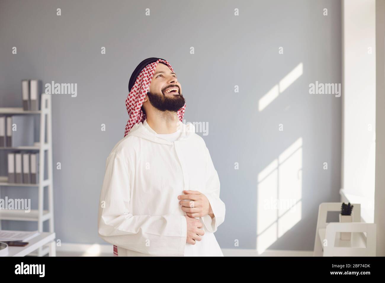Attraktiver lächelnder arabischer Mann, der lacht, freut sich, in einem modernen Büro zu stehen Stockfoto