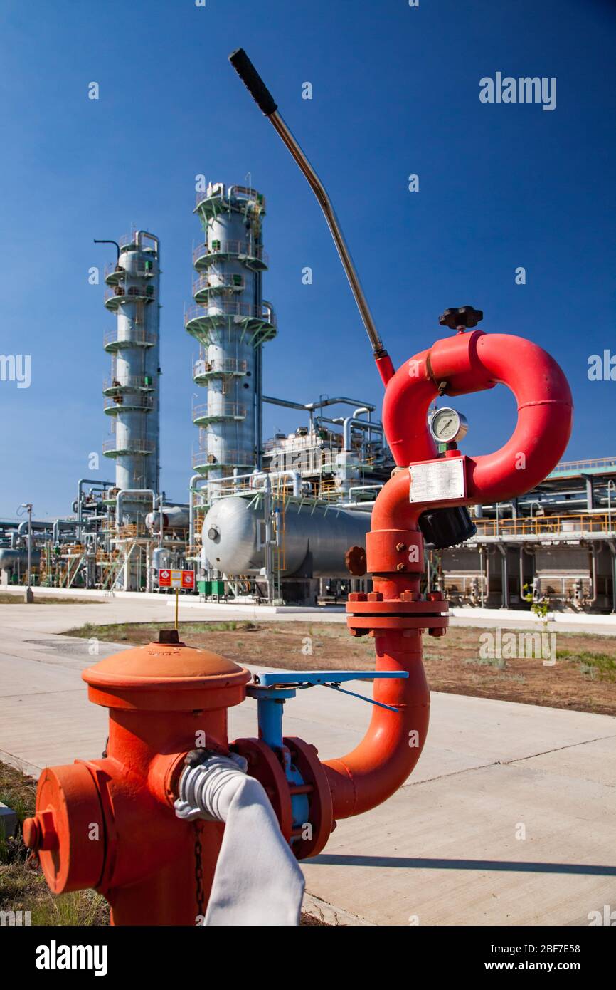 Gasverarbeitungsanlage. Ölraffinerie-Anlage. Petrochemische Anlage. Roter Feuerlöscher auf Wärmetauscher, Rohrleitungen und Destillationstürmen am blauen Himmel Stockfoto