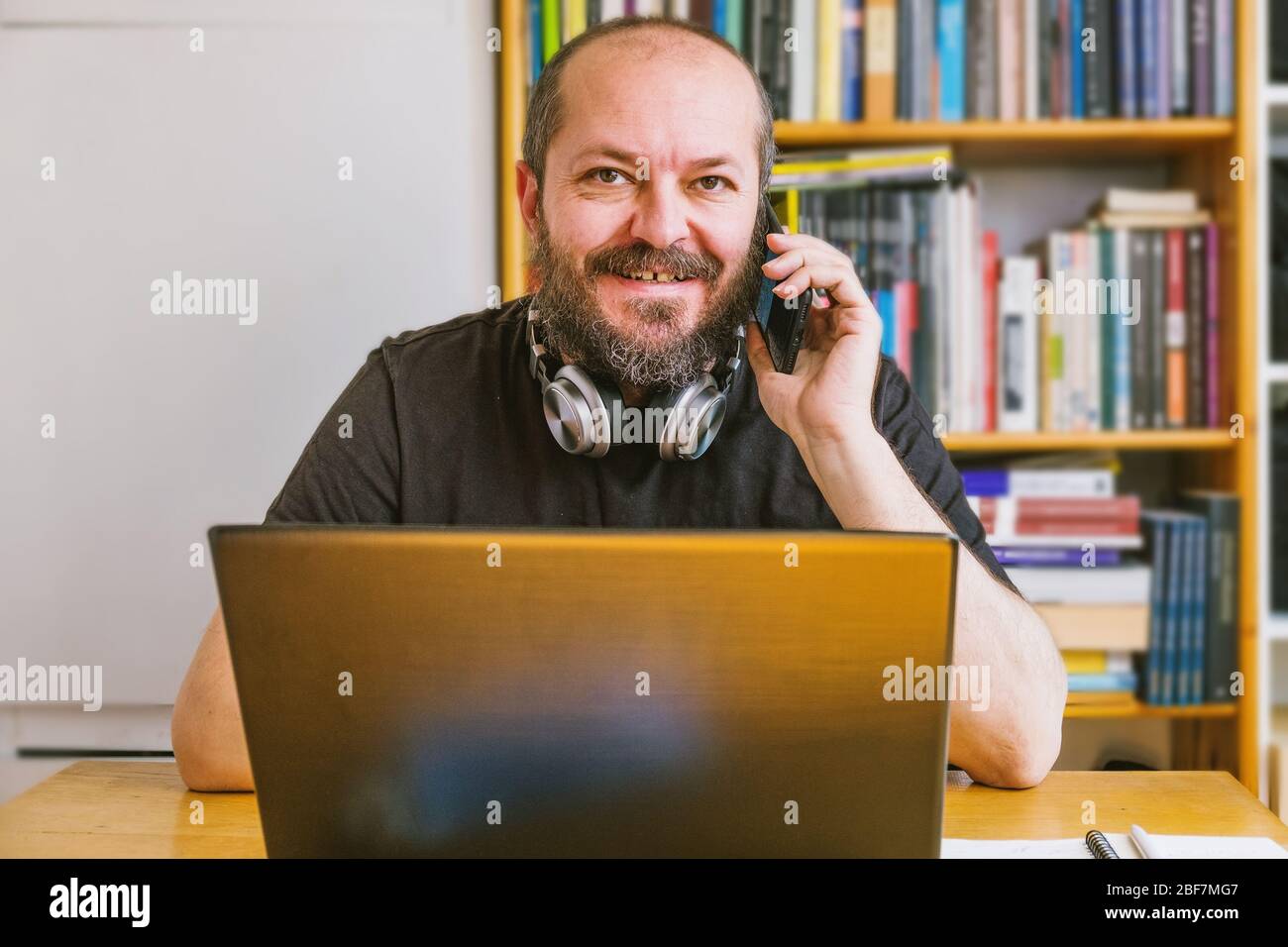Home Office-Konzept. Erwachsene bärtigen Mann konzentriert, arbeitet online von zu Hause aus auf Computer-Laptop, Bücherregale hinter ihm Stockfoto