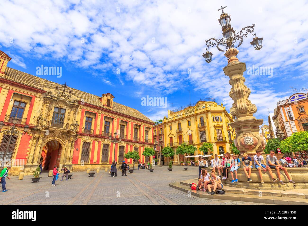 Sevilla, Andalusien, Spanien - 18. April 2016: Touristen sitzen am Brunnen auf der Plaza Virgen De Los Reyes mit dem Erzbischöflichen Palast im Hintergrund Stockfoto