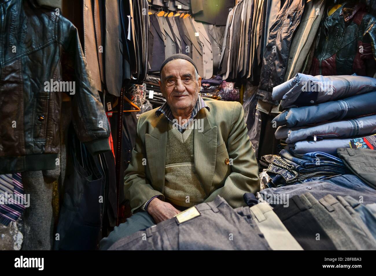 Tabriz, Iran - 22. November 2013: Iranischer Geschäftsmann verkauft Kleidung in einem kleinen überfüllten Laden im Bazar von Tabriz, einem alten Basar, der zum UNESCO-Weltkulturerbe gehört Stockfoto