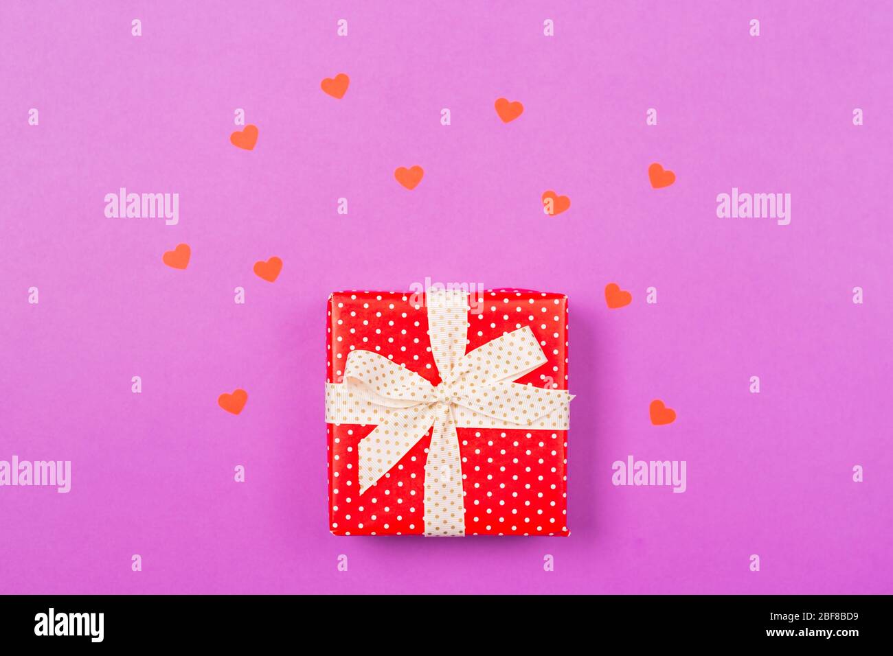 Rote Geschenk-Box mit kleinen roten Herzen um auf lila Hintergrund. Konzept des Muttertages. Konzept zum Valentinstag. Weihnachtsgeschenk. Stockfoto