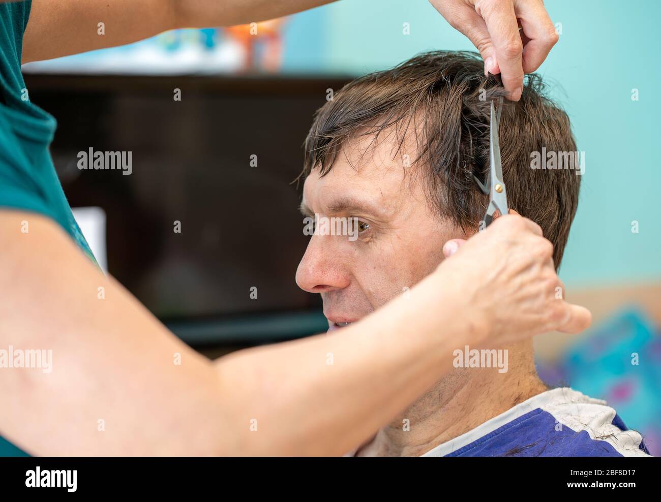 Selbsthaarpflege zu Hause während der Quarantäne. Eine Frau schneidet Haare von mittleren erwachsenen Mann die Haare zu Hause im Zimmer. Coronavirus-Pandemie. DIY und Selbstpflege concep Stockfoto