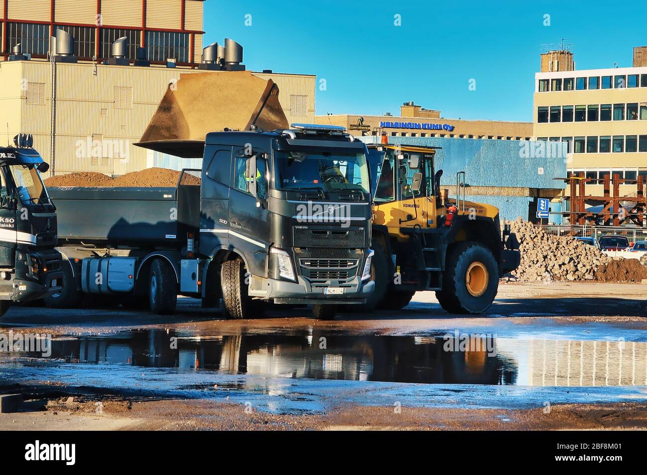 Komatsu Radlader Verladung Kies auf den Anhänger des schwarzen Volvo FH Kipper LKW auf der Baustelle an sonnigen Tag. Helsinki, Finnland. April 17, 2020 Stockfoto