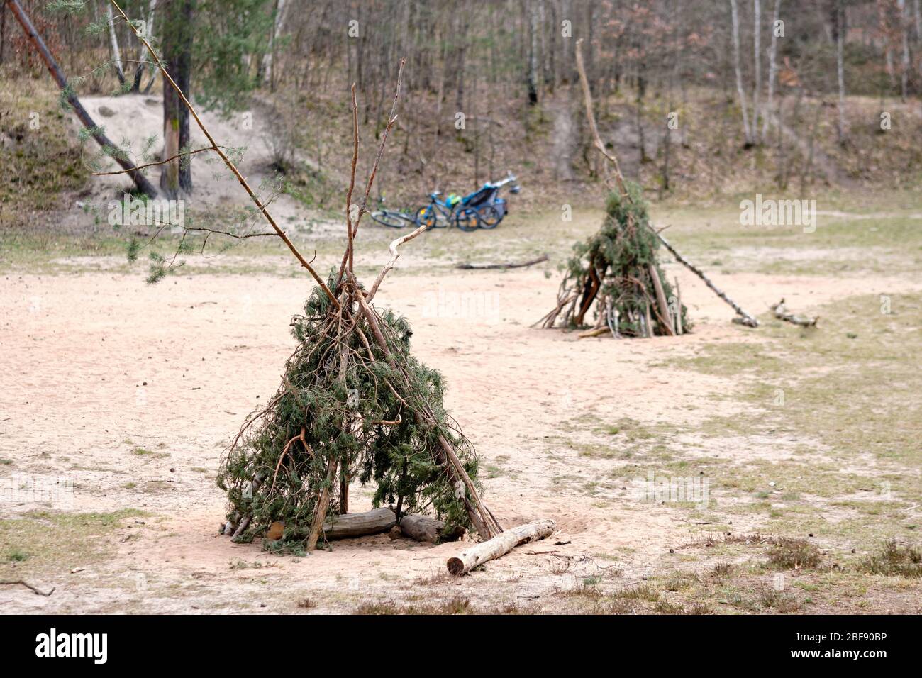 Zwei Teepis mit Zweigen und Zweigen von Nadelbäumen, die auf sandigen Grund im Wald stehen, mit Bycles im Hintergrund, die man in Deutschland im April gesehen hat. Stockfoto