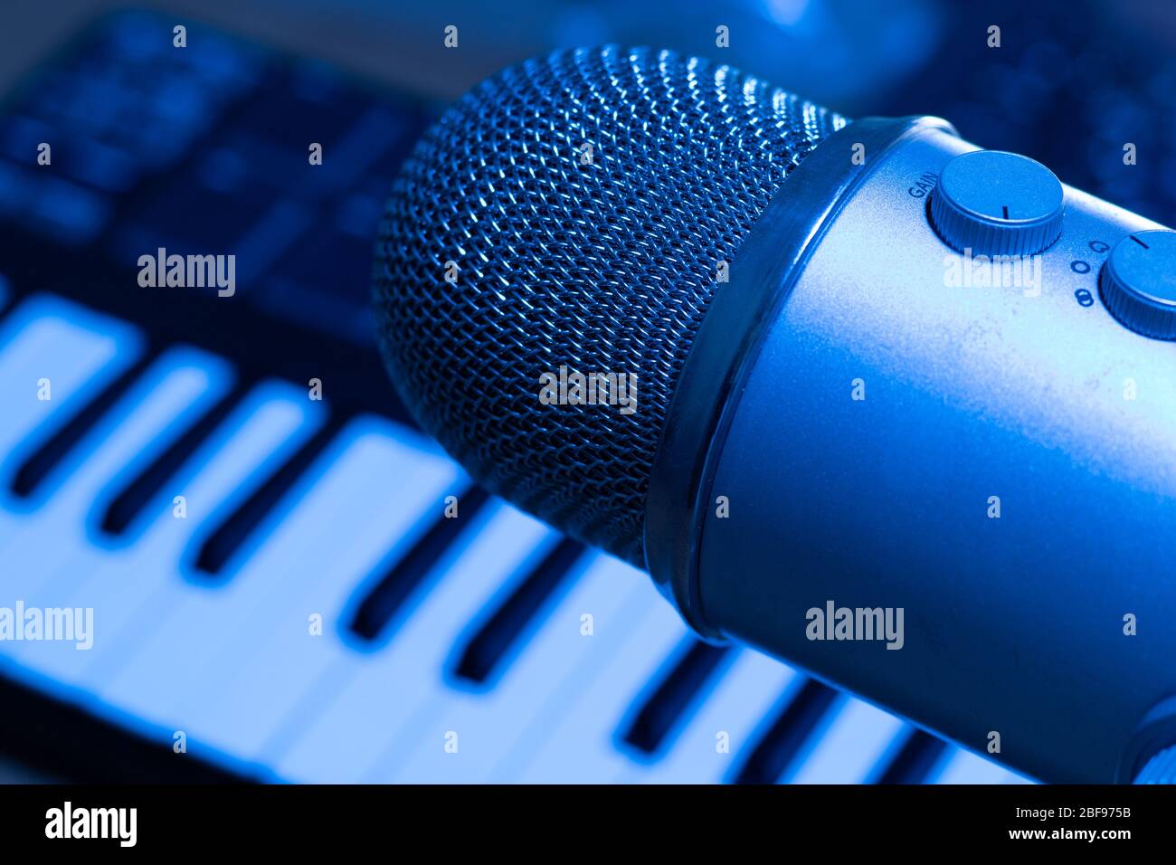 Produktionskonzept für Musiktitel. Studio mit Mikrofon und Synth-Tastatur auf Hintergrund in blauem Licht Stockfoto