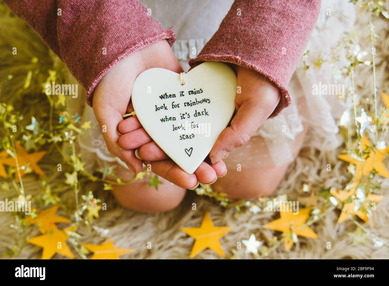 Ein Mädchen oder eine Frau, die ein Herz mit dem Zitat hält, wenn es regnet, suchen Sie nach Regenbögen, umgeben von goldenen Sternen. Coronavirus-Lockdown positive Hebung Stockfoto