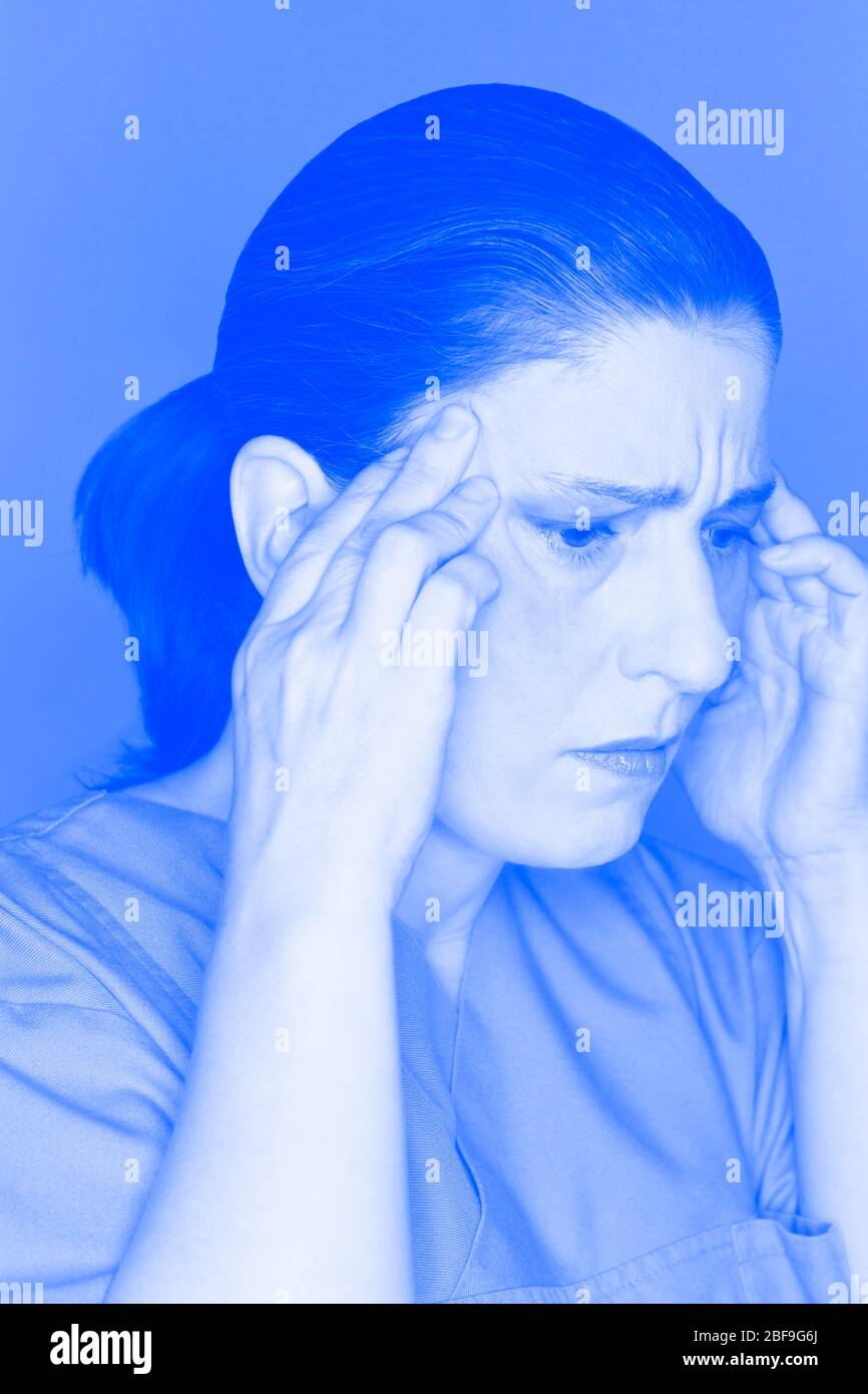 Gestresste und übermütigte Krankenschwester oder Arzt, die an einem akuten Kopfschmerzen oder Migräneanfall leidet, blauer Filter-Effekt Stockfoto