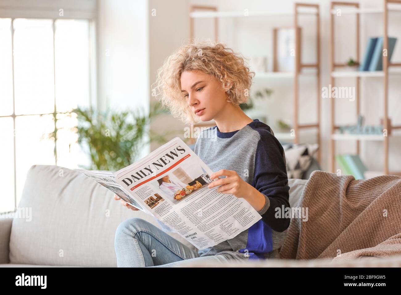 Schöne junge Frau, die Zeitung zu Hause lesen Stockfoto