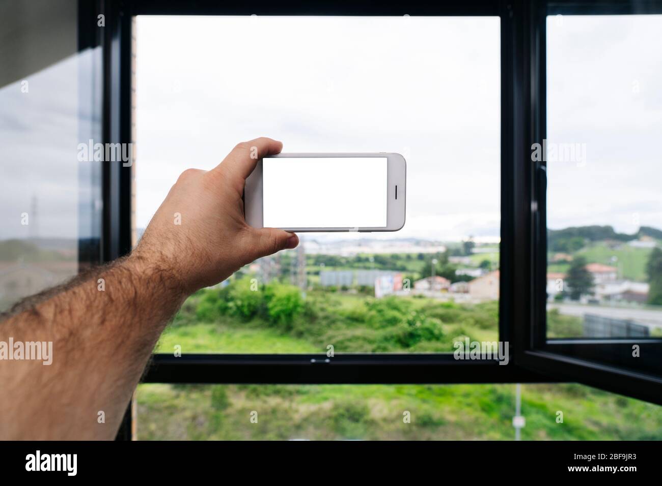 Nahaufnahme eine Hand hält ein Handy, um ein Foto aus dem Fenster eines Hauses zu machen Stockfoto