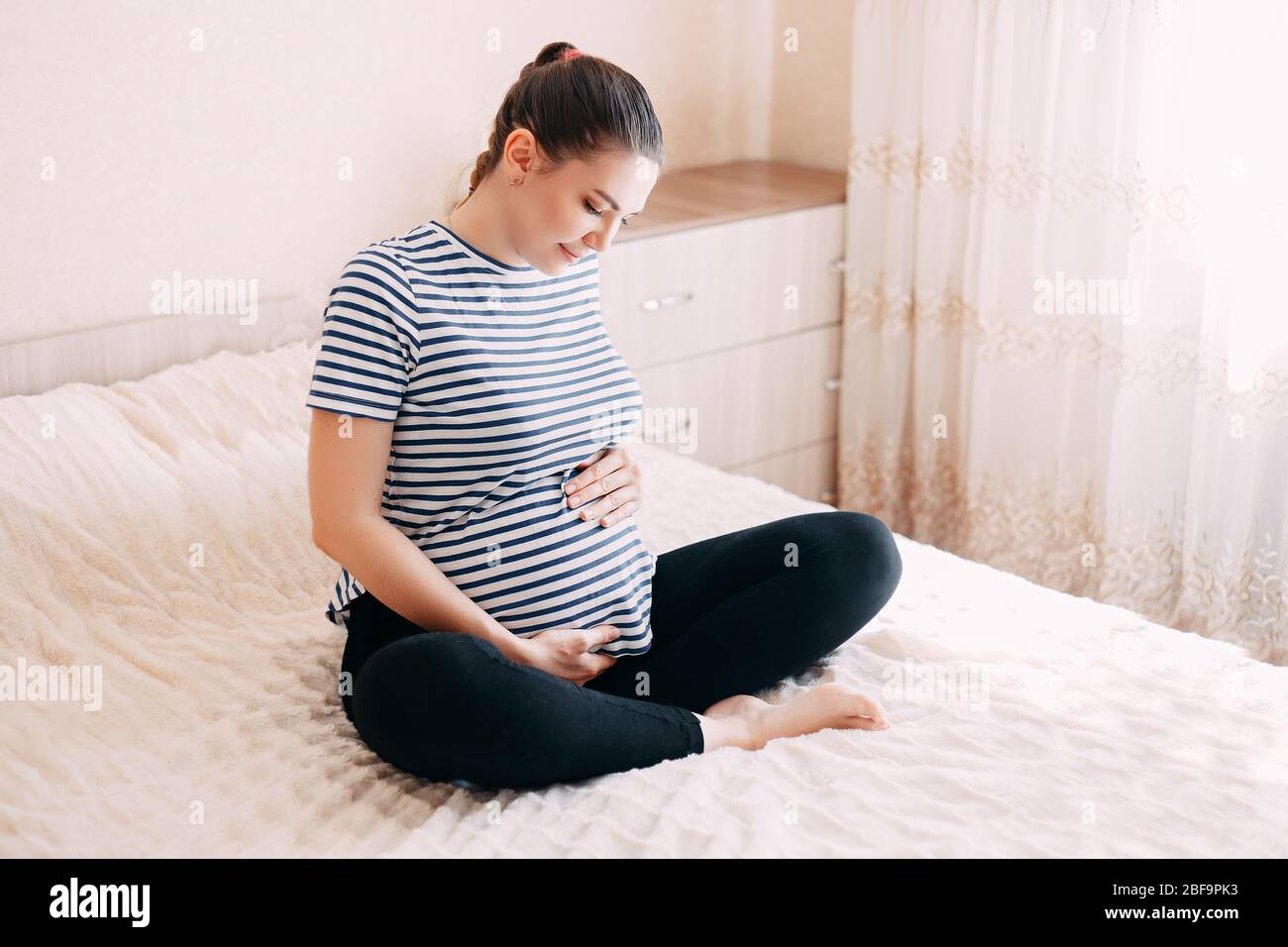 Schwangerschaft, Rest, Menschen und Erwartung Konzept - glückliche schwangere Frau am Bett sitzen und berührte ihren Bauch zu Hause Stockfoto