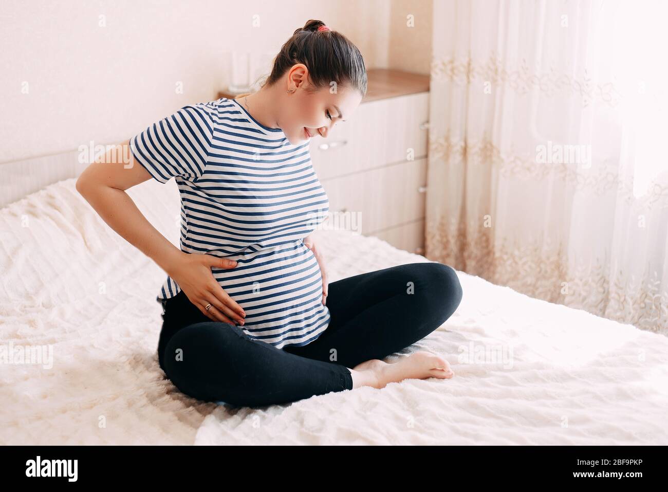 Schwangerschaft, Rest, Menschen und Erwartung Konzept - glückliche schwangere Frau am Bett sitzen und berührte ihren Bauch zu Hause Stockfoto